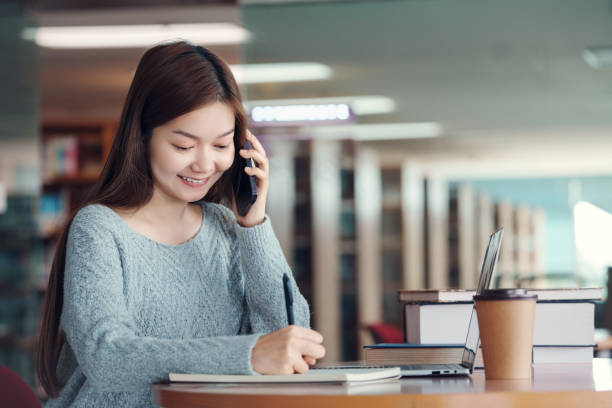 istock Happy young asian woman talking on mobile phone while sitting in library. 2064739560