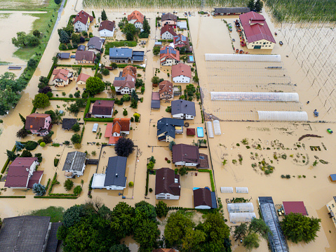 Aerial view of a suburban area affected by severe flooding, with houses partially submerged and streets inundated with water. Location: Zalec, Slovenia
