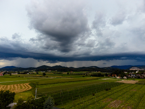 Dramatic storm clouds over a lush countryside landscape with mountains in the background.