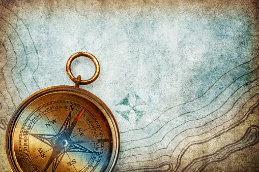 An old compass rests on top of a treasure map where X markes the spot.