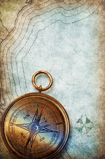 An old compass rests on top of a treasure map where X markes the spot.