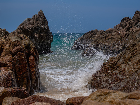 A wave crashes into the rocky shore and splashes up. High quality photo