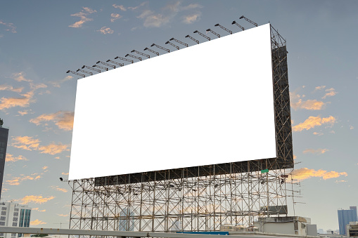 A large blank billboard against a blue sky. A blank canvas waiting for its next message. A wide shot of an empty billboard in an outdoor setting, against a blue sky with some clouds. Clipping path.