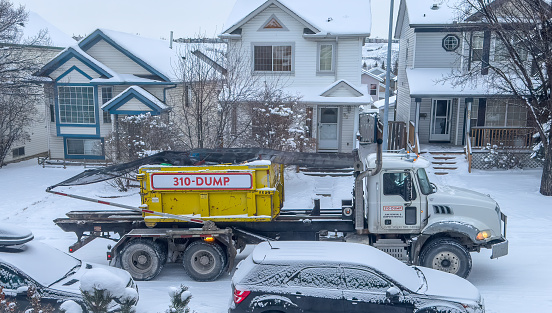 Calgary, Alberta, Canada. Mar 6, 2024. A vibrant yellow waste container affixed to a trailer, being pulled away from a residential vicinity.