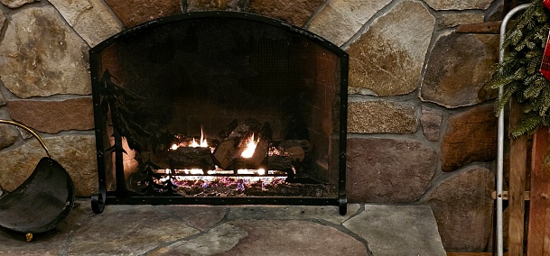 A stone wall surrounding a fireplace with the flames glowing for a cozy feel.