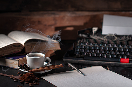 photo of a book, a steaming cup of coffee and a typewriter on a work desk