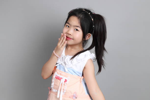 The little cut Asian girl with fancy dressed standing on the grey background.