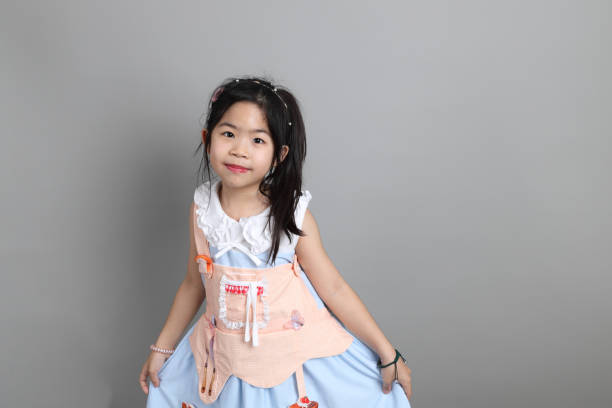 The little cut Asian girl with fancy dressed standing on the grey background.