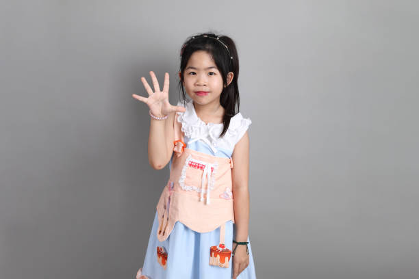 The little cut Asian girl with fancy dressed standing on the grey background.