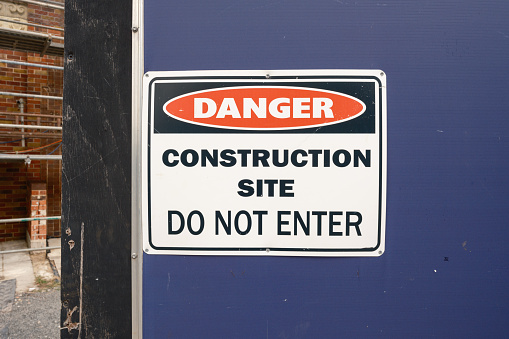 A 'DANGER CONSTRUCTION SITE, DO NOT ENTER' sign mounted on a wire fence in front of a building site