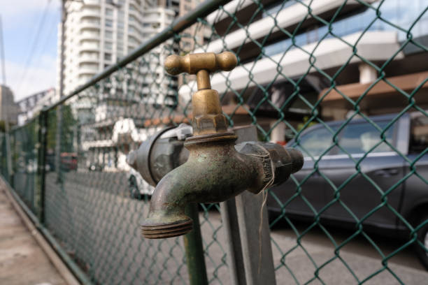 Close-up on an old brass tap on a chainlink fence along a street.