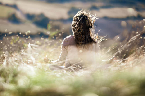 Rear view of a woman doing Yoga relaxation exercises in Lotus position during autumn day on a meadow. Copy space.