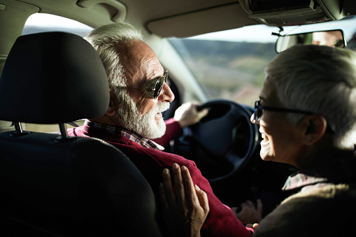 Happy mature couple communicating while enjoying in their trip in a car. Focus is on man.