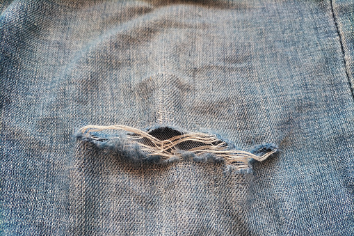 A worn-out torn leg of jeans with white fibers coming out. The concept of obsolescence and depreciation.