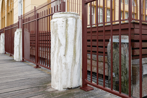 Old white wooden bollards on a pier in between metal fences.