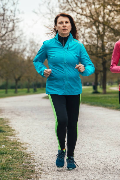 istock focused woman in blue jacket jogging in the park 2065123389