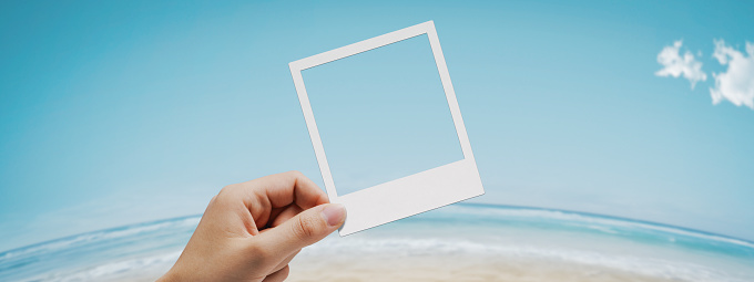 Female hand holding an instant photo and looking at the tropical beach in the background, copy space