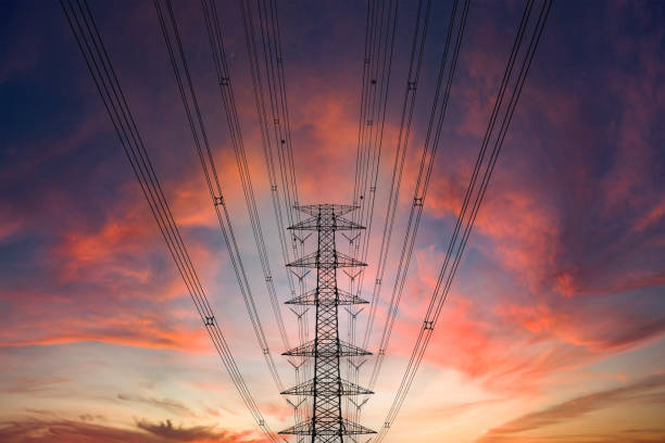 A power line crosses the foreground of a dramatic sunset. The setting sun casts a warm glow over the landscape, silhouetting.
