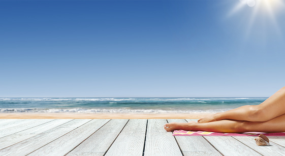 Young beautiful woman sunbathing at the tropical resort and ocean in the background, travel and summer vacations concept