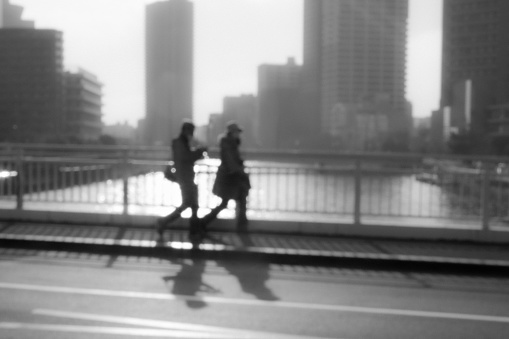 Blurry image of a couple walking on a bridge over a river in the city