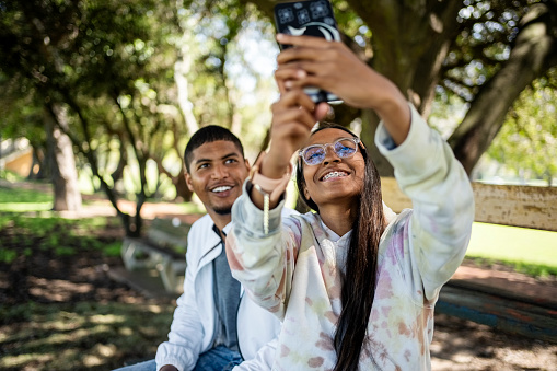 Young woman taking a selfie on her mobile phone while sitting with her male on a park bench