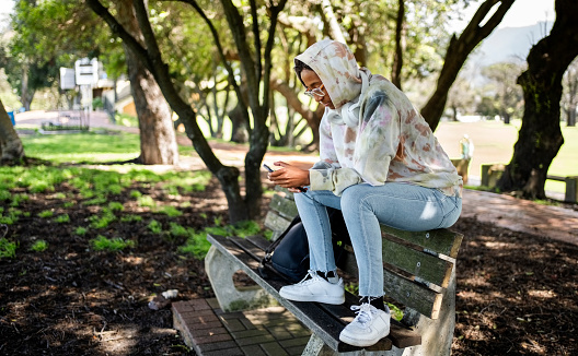 Young african girl student using smartphone while sitting on bench at college campus