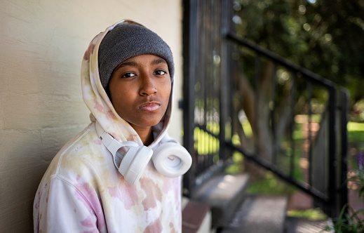 Portrait of young girl wearing hooded shirt standing by wall staring at camera outside