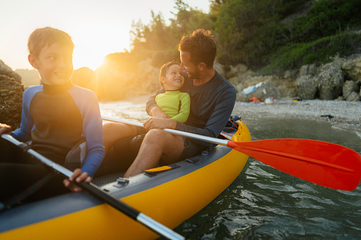 Photo of a father and his two sons practicing paddling and exploring the wild beach by kayak.