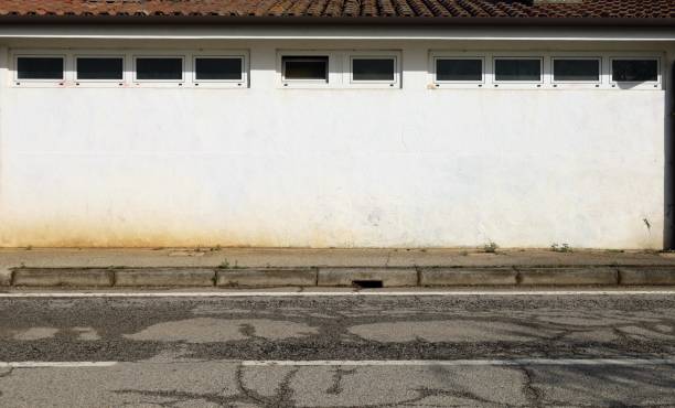 istock One floor building with white  wall and row of small windows in the upper side. Earthenware  tiles  rooftop. Concrete sidewalk and road in front. 2065203828