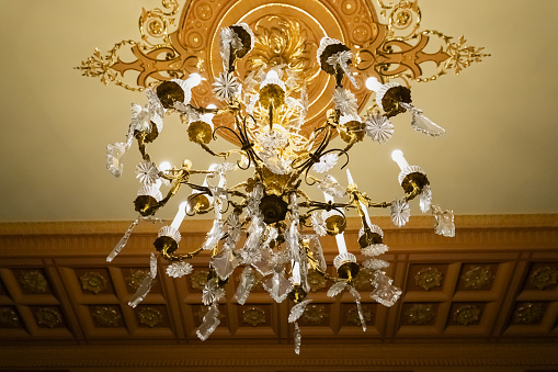 Crystal gold chandelier or luster with long electric candles on stucco ceiling at the public station in Russia, St. Petersburg. View from below