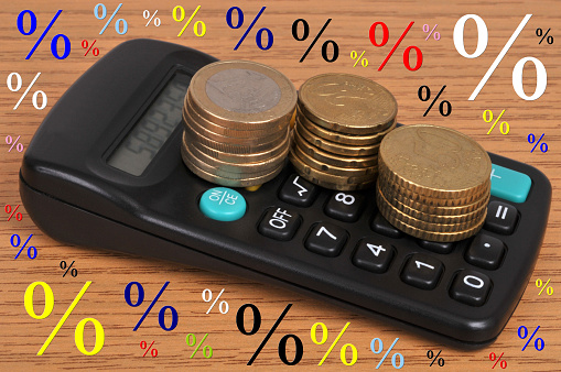Business concept with stacks of Euro coins lying on a calculator surrounded by percentage signs