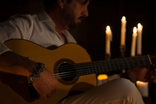 Spanish person playing the classical guitar. The man is illuminated by candlelight.
