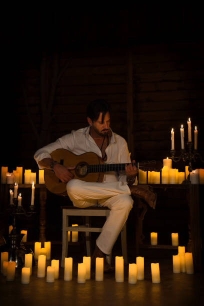 istock Man dressed in white enjoying playing the Spanish guitar at home by candlelight, learning a musical instrument. Vertical photo. 2065220448