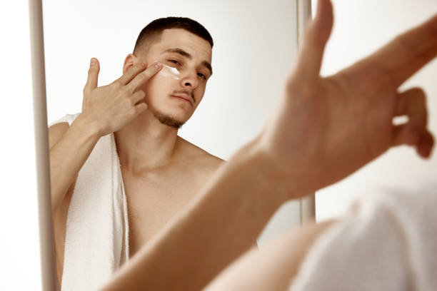 istock Young man in bathroom looking in mirror and moisturizing face after shaving. Selective focus 2065240349