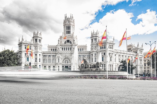 Timelapse at statue in the Plaza de Cibeles with the representation of the goddess of the same name and two lions with Spanish flags waving in the wind behind and traffic