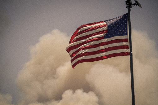 American flag waving in the air with smoke billowing from a house