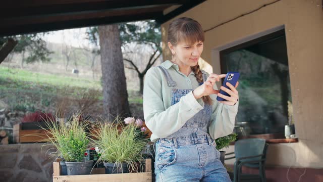 Female gardener uses her phone standing on the terrace of a country house