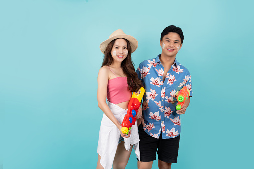 Portrait of Young Asian couple in summer outfits and holding water gun isolated on blue background with copy space. Songkran festiva.