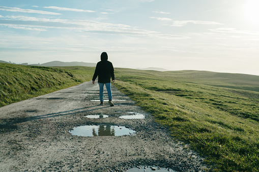 A man walking on a dirt road with pot holes