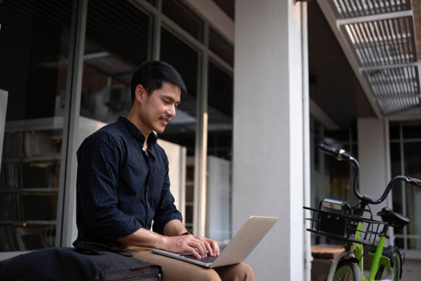 istock A young Asian businessman rides a bicycle to work. Use a reusable water bottle. Working outside of the office using a laptop The concept of saving energy and reducing pollution to the environment. 2065307321