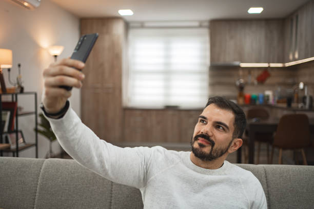 istock Man taking selfies on mobile phone while relaxing on sofa at home 2065328751
