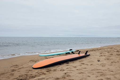 A shot of two surfboards lying on the sand on a beach in Northumberland, North East England. It is an overcast summer's day and the sea is calm, small waves rolling into shore.