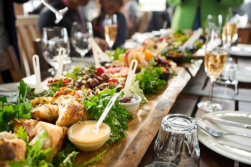 Assortment of delicious food sitting on wooden platters on a table with wine glasses during a dinner party