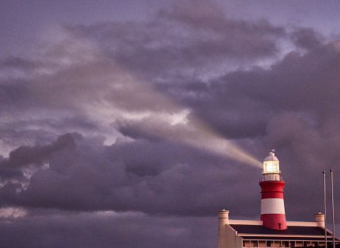 Lighthouse shining its lantern against a dramatic sky at dusk