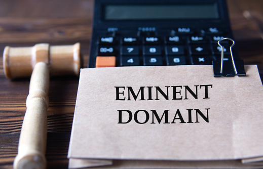 EMINENT DOMAIN - words on light brown paper against the background of a calculator and a judge's gavel