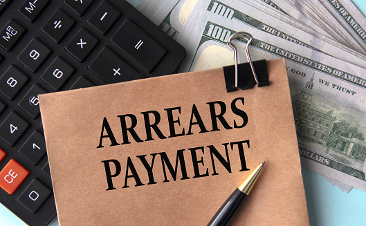 ARREARS PAYMENT - words on brown paper on the background of calculator and banknotes. Business concept