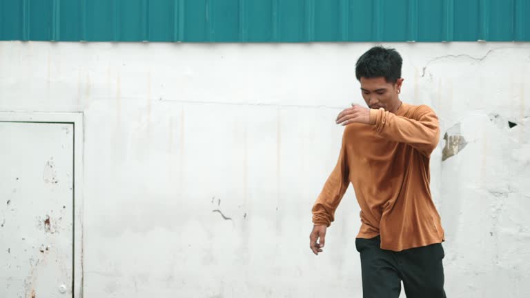 Hispanic man stretch arms and perform street dancing in front of wall. hiphop.