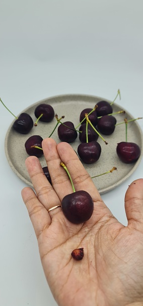 Hand is holding seed and fruit of tasmanian cherry fruit, with background of tasmanian cherry fruits served in a small plate, isolated on white background.