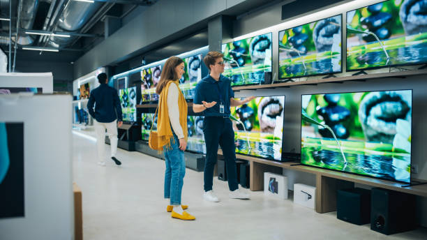 istock Beautiful Female Client Having a Conversation with Retail Home Electronics Shop Consultant. Young Woman is Shopping for a Modern TV Set. Customer Looking for a New Television in Department Store 2065387758