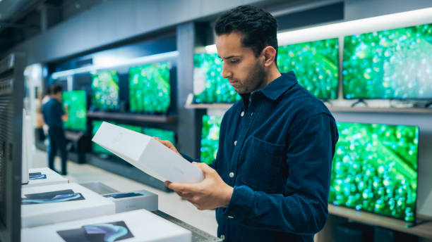 istock Handsome Young Man Shopping for a Tablet Computer in a Home Electronics Store. Multiethnic Customer Comparing Different Technology Features, Sale Price and Battery Life on a New Device 2065392225